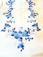 White cotton tablecloth with blue floral appliqué embroidery arranged in a symmetrical, decorative pattern.