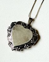 Close-up front view of large vintage sterling silver heart locket showing smooth heart center with floral motif border and attached chain loop.