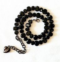 Full view of the black oval faceted glass crystal necklace coiled with extender chain and heart charm visible.