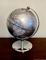 Front view of silver globe showing South America and Atlantic Ocean on reflective metallic surface with polished silver base.