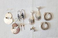 All five pairs of sterling silver earrings arranged on white background, showing variety of shapes and styles.
