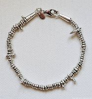 Full bracelet laid flat showing round stacked silver beads and small drop-shaped silver dangles with lobster claw clasp