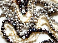 Close-up photo showing three strands of natural pearls in cream white, dark black with iridescence, and grayish colors, highlighting the knotted ends and irregular shapes.