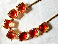 Close-up of the seven square-cut amber to rose pink glass stones with gold-plated settings showing faceted cuts and intricate prongs.