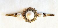 Front view of the bar brooch showing gold-tone metal, central faux pearl surrounded by clear rhinestones and two smaller pearls on each side.