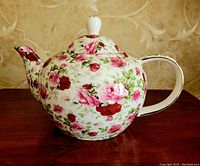 Front side view of the round floral rose bud patterned teapot with lid, showing the spout and handle with gold accent.