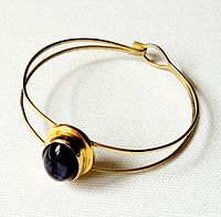 Front angle showing the gold-tone double wire bangle with large polished purple glass cabochon centerpiece.