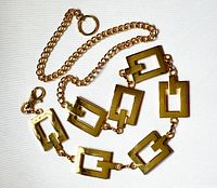 Full view of the gold-tone link chain belt laid in a circle showing lobster clasp and chain extension.