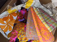 Close-up of assorted fabric remnants showing various colorful and retro patterns in vibrant oranges, pinks, browns, and beige.