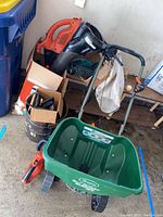 Photo showing Scotts Turf Builder fertilizer spreader, Black & Decker leaf blower, some garden clippers and sprayer in garage corner.