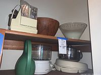 Shelf view showing Sunbeam food processor, large teak bowl, glass bowl, metal bowl with lid, and vegetable dip server under shelf