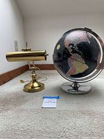 Desk lamp and Encyclopedia Britannica globe side by side on carpeted floor near wall
