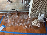 Multiple clear glass wine and aperitif glasses arranged on wooden floor with partial view of outdoor area and nearby furniture.