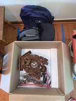 Top view of cuckoo clock and travel items inside box and on floor including backpack, lunch box, and travel pillow
