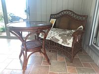 Front view of the loveseat and round bamboo-style table on tiled porch showing cushion and table glass top