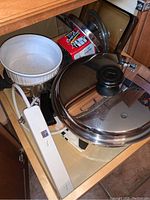 Drawer containing CorningWare casserole with lid, Prestige pot with lid, red Coop cup, power strip and visible slow cooker cord at bottom
