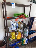 Full view of five shelf wooden shelving unit holding various garden and garage supplies including multiple bottles, bags, and tools.