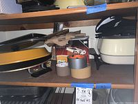 Photo of shelf with yellow electric round griddle, white electric roaster, assorted tape rolls, cookie sheets and serving trays.