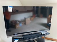 Front view of Sony Bravia TV showing full screen, stand, and two remote controls.