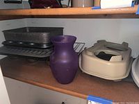 Shelf with 2 metal baking pans stacked, large purple vase, and beige heated pet feeding bowl
