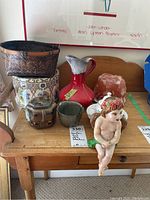 Overview of all ceramics, statue, basket, and tin on wooden table including Ainsley sugar bowl set, jug, and angel statue.