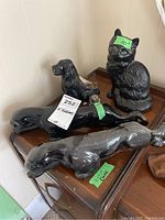 Overview photo showing two elongated black porcelain jaguars, black seated dog figurine, and black metal cat figurine on wooden surface.