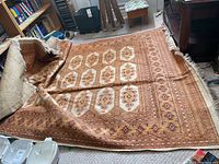 View of the folded and spread rug showing central geometric medallions and detailed borders, placed in a room with furniture.