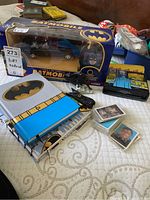 Photo shows boxed Batmobile, Batman sketch pad and lined notebook, boxed Batman and Batmobile figures, and Batman holographic collector cards spread on a bed.