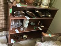 Front and side angled view of wooden bookcase with decorative beaded trim, showing three shelves filled with various items.