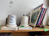 Pair of white marble bookends with column design on wooden shelf, holding books upright