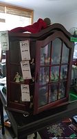 Miniature curio cabinet with glass pane door and multiple shelves visible, wooden gavel placed on top, various miniature figurines inside the cabinet (not included)