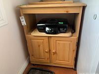Front view of wooden cabinet showing the open shelf with an electronic device on top, and closed double-door storage below, with caster wheels visible.