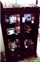 Front view of dark wood cabinet with two glass doors revealing four shelves inside, holding various glass and ceramic items (not included).