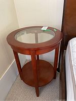Front view of round wood end table with glass top showing the overall structure and condition.