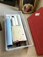 Rolled posters stored in a clear white plastic bin, showing varied paper types and sizes.