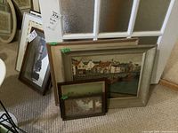 Stack of framed art prints leaning against a glass door, showing multiple sized framed prints; two main visible prints are a harbor scene and a classical figure scene.