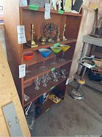 Front and side view of wood bookcase with glassware and brass items on the shelves.