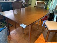 Angle showing full view of wooden dining table with chairs around it on a wooden floor.