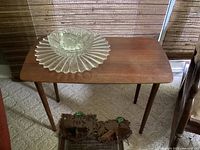 Full view of a wooden table holding two clear glass dishes, showing wear on the table surface and carpet flooring beneath.