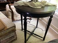 Full view of round wooden table with crocheted tablecloth on top, showing dark finish and carved details.
