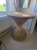 Full view of the wicker hourglass shaped table next to a window and curtains