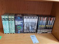 Photo showing the full lot on a wooden shelf, featuring several boxed VHS tapes with titles visible including The Hitchhiker's Guide to the Galaxy and Twin Peaks.