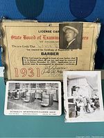 Close-up photo showing the 1931 State Board of Examiners barber license card with small portrait photo attached, along with two vintage black and white photographs (Russell's Sportsman's Barber Shop and barber working outdoors).