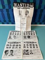 Full set of six smaller wanted posters arranged in two rows with one larger wanted poster of Quay Cleon Kilburn standing upright behind them on a blue surface with blue patterned background.