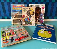 Seven 1960s vintage hardback children’s books stacked and standing, showing colorful covers from Peanuts, Richard Scarry, and Carol Baker.