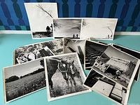Assorted vintage black and white photographs arranged on a surface showing various subjects including farmland, horses, architectural structures, and outdoor scenes.