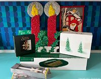 Lot of holiday and vintage decor items including 2001 Georg Jensen ornament in original box, Department 56 trees and table grass packages, vintage popcorn-shaped candles, and decorative fabric card holder and box.