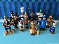 Full view of 14 wooden German incense smoker figurines in various styles and colors on blue background.