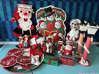 Full view of the Mid Century Christmas decor items showing Santa stuffed figure, chimney drawer box, candle holders shaped like Santa legs, felt road signs, elves, and holiday tray.