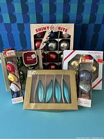 Photo showing full lot including original Shiny Brite box of 12 ornaments, Woolworth style disc ornaments in packaging, red Shiny Brite ornament case, and other assorted boxes of metallic glass ornaments in silver and blue-green tones.